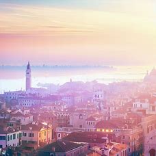 Craft a stunning view of Venice at sunrise, with pastel hues illuminating the city and a view of the lagoon sparkling in the background.