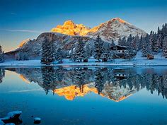 Snow Covered Pine Trees And Yellow Covered Mountains Reflection On Lake ...