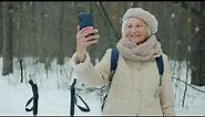 Beautiful senior lady taking selfie in winter park using smartphone camera smiling posing