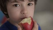 Cute Little Boy Eating Red Apple. Child Eats Fruit. Kid Bites Fruit and Chews Looking at Camera in Kitchen. Healthy Diet Vegetarian. Healthy Nutrition Child Development. Happy Boy Biting Eating Apple.