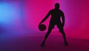Free stock video - Studio silhouette of male basketball player dribbling and bouncing ball against pink and blue lit background