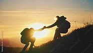 Silhouette of a helping hand to the man mountaineer. Two hikers on top of the mountain, a man helps a man to climb. Two hiker helping on hiking trail to summit the top of mountain. Teamwork concept.