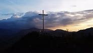 Aerial View of a Religious Christian Steel Cross on a Hill in the Mountainous Countryside in Sunset