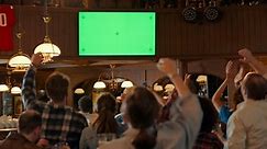 Group of Multicultural Friends Watching a Live Sports Match on TV with Green Screen Display in a Bar. Happy Fans Cheering and Shouting, Celebrating When Team Scores a Goal and Wins the Tournament.