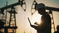 Oil pump.Engineer work with laptop and diagram.Checking operation of oil pump at plant.Silhouette of man in an industrial area.Silhouette of an engineer checking operation of an oil pump in desert