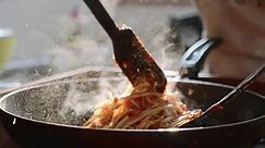 Cucinare e mescolare gli spaghetti con salsa di pomodoro rosso nella padella, primo piano al rallentatore