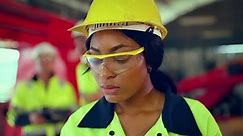 Portrait of woman looking camera at manufacturing special facility. Attractive women industrial engineer wear safety helmet, processes orders and products at manufacturing plant then look at camera.