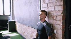 Male fitness instructor does wall sit exercise at gym. Wall sits to make hip and thigh stronger. Effective exercises for running. Short flexibility-focus session at workout place.