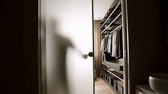 The silhouette of a man opens the door to the dressing room.Row of men suit jackets on hangers. Collection of new beautiful clothes hanging on hangers in a shop . Home Wardrobe with Clothing.Door Open