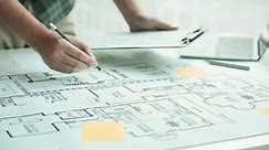 Interior designer or architect reviewing blueprints and holding pencil drawing on desk at home office.