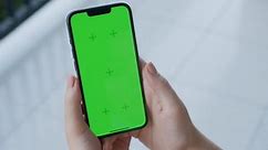 Point of View of woman holds mobile phone iPhone and watching a video on the background of a floor with white tiles. Use green screen for copy space closeup. Chroma key mock-up on smartphone in hand.