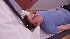 Mid aged chiropractor examining neck joint of young adult male
