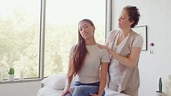 Professional female chiropractor adjusting her patients spine and back while she sits on a bed in the office. Tense woman receiving a relaxing spine realignment at a spa from a health practitioner