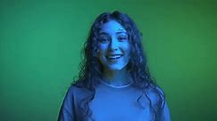 Happy Portrait of Young Woman Looking at Camera and Smiling in Neon Color of Shining Filter. Multicolor UV Effect of Backlight Illumination Inside Studio. Amazing Person with Toothy Grin and Long Hair
