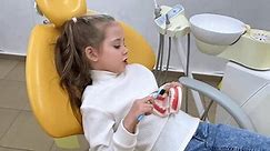 Little girl is practicing how to properly brush her teeth. Good oral hygienist with jaw model teaching patient to clean teeth properly to prevent caries, keep teeth healthy and have beautiful smile.