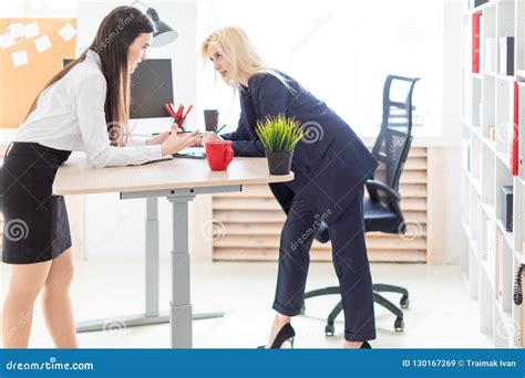 two girls stand in the office bent over near the table and work with