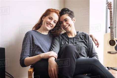 Happy Lesbian Couple Sitting On Chair At Home Stock