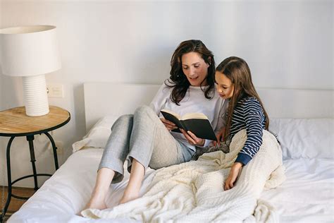 Mom And Her Daughter Reading A Book On Bedroom In The Morning By