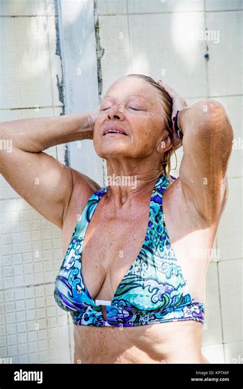 Older Retired Senior Caucasian Woman Showering At The Beach In A Blue