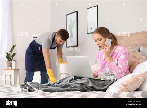 Busy Wife Working On Bed While Her Husband Doing Chores At Home Stock