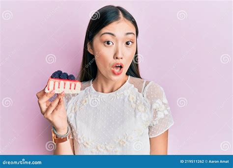 Young Chinese Woman Eating Cheesecake Scared And Amazed With Open Mouth