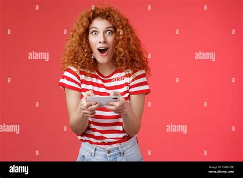 Impressed Excited Good Looking Redhead Curly Woman Hold Smartphone