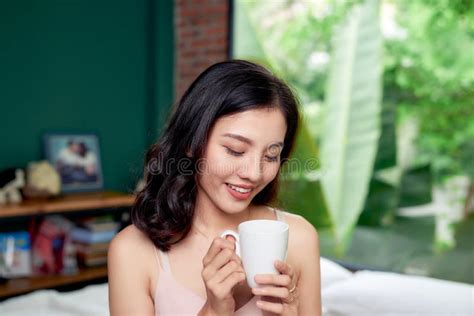 Smiling Woman Drinking A Cup Of Coffee In Bedroom In The Morning Stock