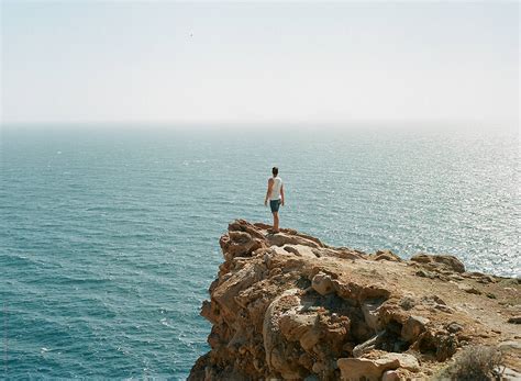 man standing   edge   cliff overlooking  ocean  stocksy