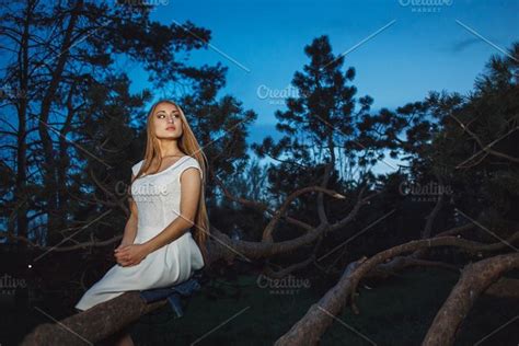 beautiful blonde girl sitting on old tree branch in mystical fairy