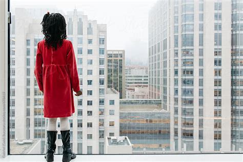 african american girl looking out of a tall building window by gabriel