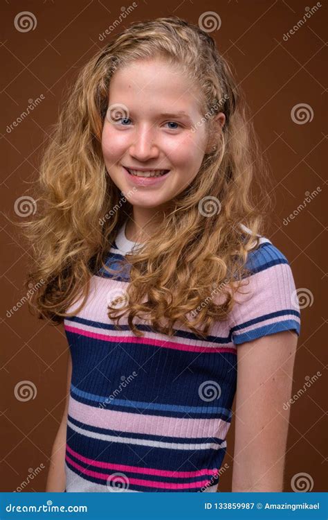 Young Beautiful Blonde Teenage Girl Smiling Against Brown Background