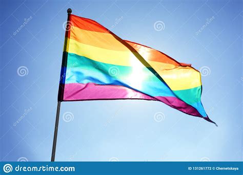 rainbow lgbt flag fluttering on blue sky background stock
