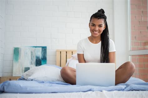 bonne jeune femme avec un ordinateur portable assis dans son lit télécharger des photos