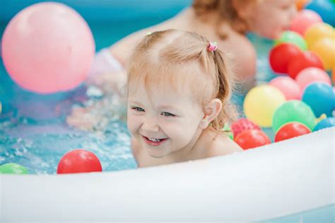 mała dziewczynka bawi się zabawkami w nadmuchiwanym basenie w słoneczny