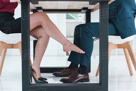 cropped shot of businesswoman flirting under table with businessman in