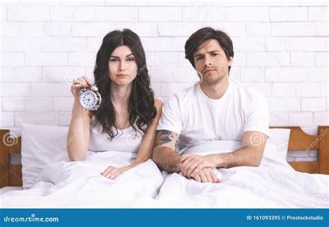 Sleepy Couple Sitting In Bed With Alarm Clock In Morning Stock Image