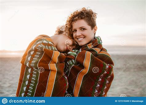 Smiling Lesbian Couple Wrapped In A Beach Blanket At Sunset Stock Image