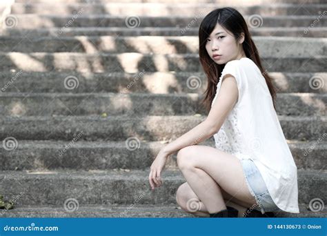 cute asian woman in a white top squatting down on steps stock image