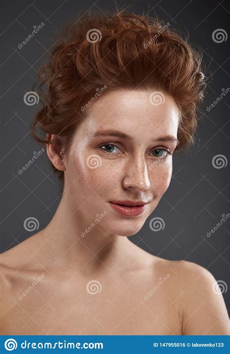 beautiful red haired girl with freckles posing against gray background