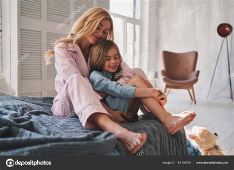 Beautiful Blonde Mother Embracing Her Daughter Smiling While Sitting