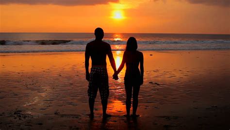 silhouetted couple holding hands on the beach in the sunset stock