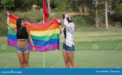 Spanish Lesbian Couple Posing In A Golf Field With A Pride Flag Stock
