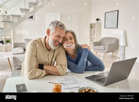 Happy Mature Older Couple Laughing Bonding Sitting At Home Table With