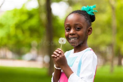 Outdoor Portrait Of A Cute Young Black Girl Blowing A Dandelion Stock