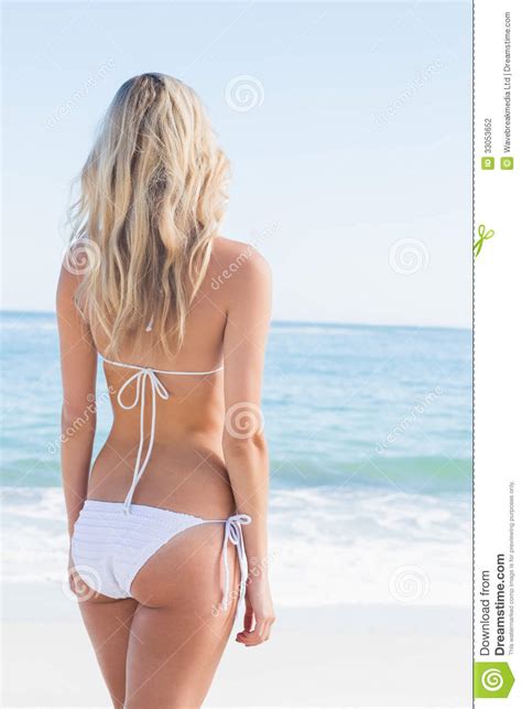beautiful blonde in white bikini looking at the sea stock