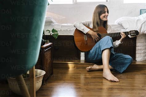 Barefoot Woman Sitting On The Floor In Front Of Bed Playing Guitar