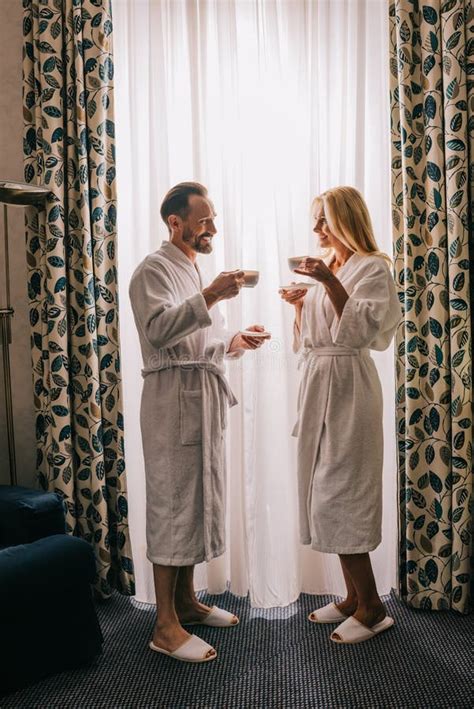 Side View Of Happy Mature Couple In Bathrobes Drinking Coffee And