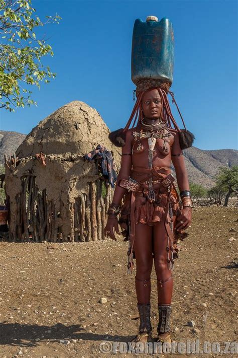 an african woman in traditional garb and headdress stands outside her