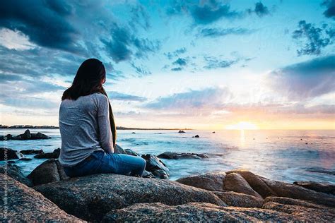 Woman Sitting On A Rock Enjoying A Beautiful Sunset View Over The Sea