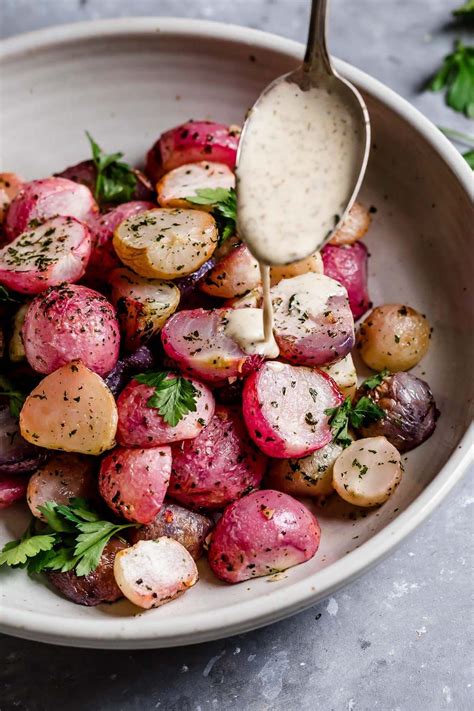 a white bowl filled with red potatoes and parsley next to a spoon full